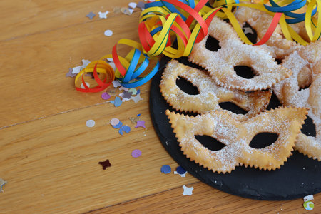 Traditional sweet crisp pastry deep-fried in shape of Carnival mask on a black slate stone plate. Chiacchere or crostoli, bugie, cenci with copy spaceの写真素材