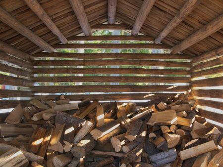 Building for storing firewood made of wooden logs. Space between the logs reveals early spring forest background with the trees, reminders of snow and warm sunshineの写真素材