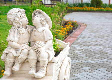 Photo of kissing statues of a boy and a girl in a city park among green plantationsの写真素材