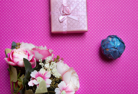 A flat lay photo of a bouquet of flowers, a gift in the form of a box and accessories on a pink...
