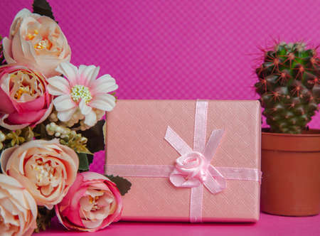 A photo of a bouquet of flowers, a gift in the form of a box and a cactus on a pink background, front view. High quality photoの写真素材
