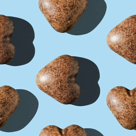 Photo in the form of a seamless pattern. Chocolate gingerbread in the shape of a heart of dark brown color with shadows on a colored light blue background.の写真素材