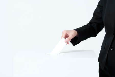 A woman's hand in a suit putting paper in an election ballot boxの写真素材