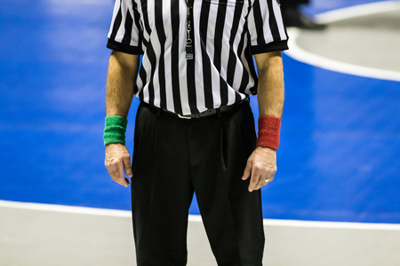 Male wrestling referee wearing red and green wrist bands and black and white striped shirt.の写真素材