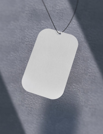Blank white price tag hanging on gray wall with shadow and sunlightの写真素材