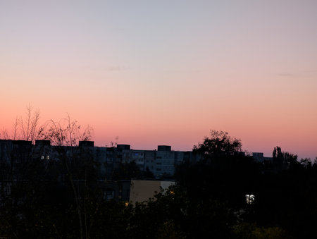 Sunset in the city with silhouette of houses and trees in the foregroundの写真素材