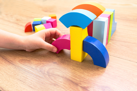 A child plays with colored blocks, colored cubes constructs a model on a dark wooden background.の写真素材
