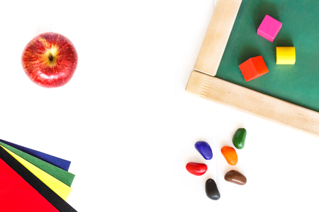 School board, colored blocks, red apple, wax crayons, colored paper lying on a white wooden background.の写真素材