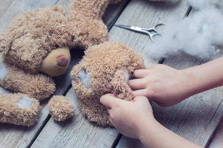 A girl sews a bear toy. Handicraft with children. Child fills the toy with a sintepon.の写真素材