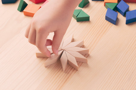 A child plays with colored blocks constructs a model on a light wooden background.