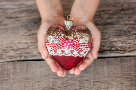Christmas tree toy heart in the hands of a child. New Year. Christmas. Wooden Background. Toning lightの写真素材