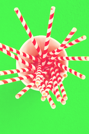 Red straws for juice in a paper cup on a greenの写真素材