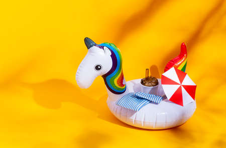 Inflatable unicorn toy. Beach vacation concept. Sea, umbrella, drink, palm shadows, happiness and joy.Yellow backgroundの写真素材