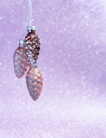 Pink mother-of-pearl 3 cones hang from ribbons. Christmas card on a lilac shiny background.の写真素材