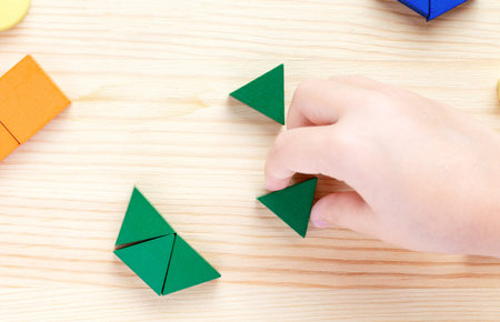 A child plays with colored blocks constructs a model on a light wooden backgroundの写真素材