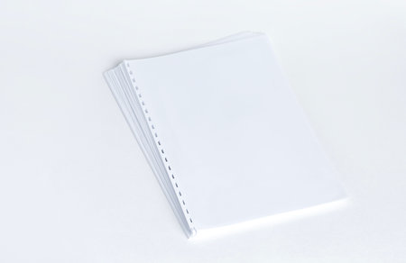 Blank sheets of paper with punched holes prepared for binding works with a plastic spiral on a white background. Mockupの写真素材