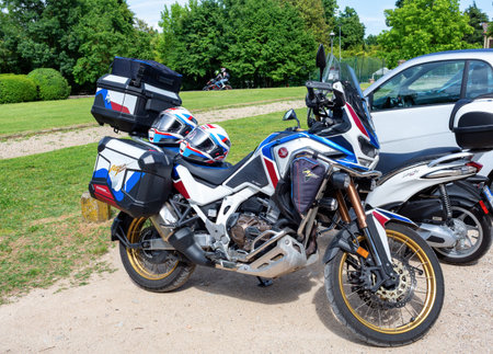 Galzignano Terme, Padua, Italy-May 17, 2025 : Adventure motorcycle Honda parked, equipped with colorful saddlebags and helmets, surrounded by green trees and grassの写真素材
