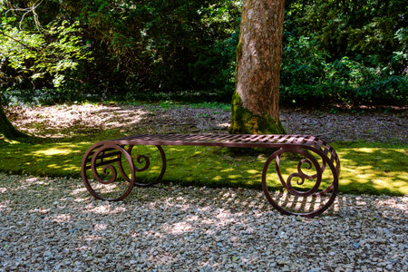 Decorative metal bench with intricate scrollwork design placed on gravel surface surrounded by lush greenery and trees in Villa Barbarigo Valsanzibio Padua Galzignano Terme.の写真素材