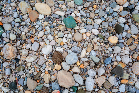 Diverse collection of smooth stones and pebbles in various colors and sizes, creating a textured...