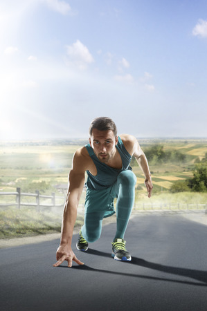 Running athlete man. Male runner sprinting during outdoors training for marathon run. Athletic fit young sport fitness model in his twenties in full body length on road outside in nature.の写真素材