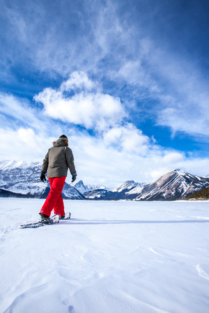 Young woman snowshoeing on a frozen lake in the Canadian Rocky Mountains, Kananaskis, Alberta, Canadaの写真素材