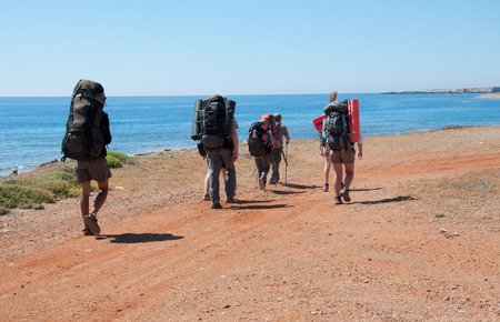 A group of tourists with large backpacks are on the sandy road to the seaの写真素材