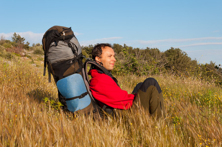 Tired out tourist  with backpack is sitting on stone in meadow and watching into misty valley. Autumn misty day in mountains.の写真素材