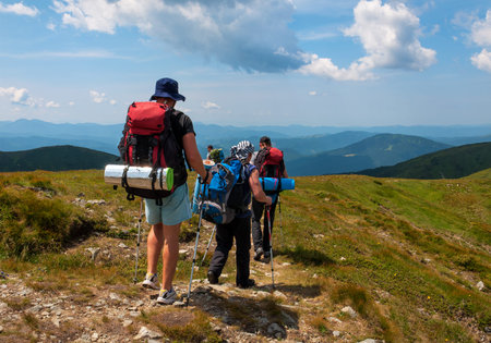 A group of tourists with large backpacks are on the sandy road to the mountain
