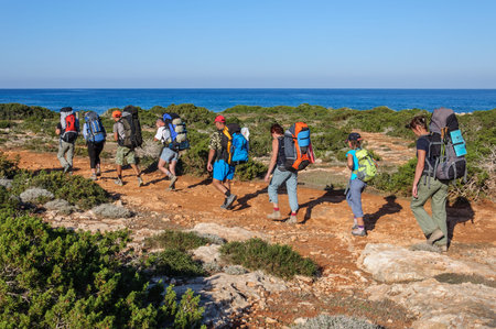 A group of tourists with large backpacks are on the sandy road to the sea