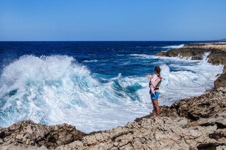young woman with child stands on stone precipice and looks at a storm on the Mediterranean Sea