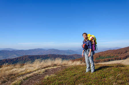 A sporty happy mother with a small daughter in a backpack carrying walks in the mountains of the Carpathians. Ukraine. Europeの写真素材