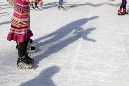 Parent and child Ice Skate together outdoors, along with their shadows.のeditorial素材