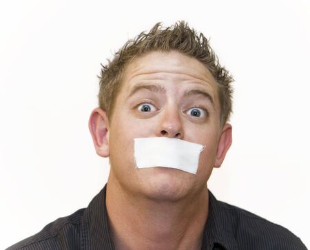 Early 20s man mug shot with wide eyes and a piece of tape over his mouth. White background.の写真素材