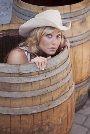 Young cowgirl peeking out of a barrel with a worried look on her face.の写真素材