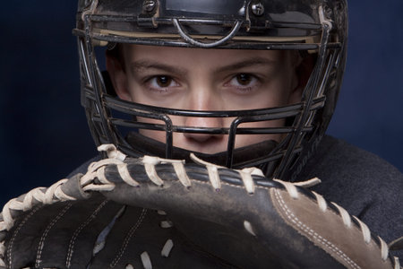 Young teenage boy in catcher's mask with glove ready and dramatic dark blue background.