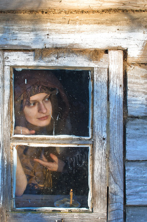 beautiful peasant woman wrapped in a woolen shawl with an insidious smile looks out into the window of the house, something she was interested inの写真素材