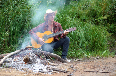 cowboy plays guitar sitting by the fireの写真素材