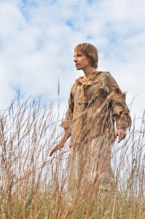 young man dressed as a medieval peasant amidst wild yellowed ears against a blue skyの写真素材