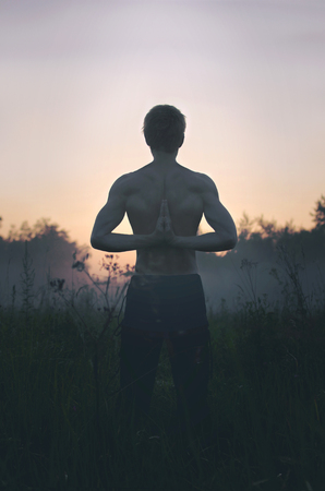 young man with hands folded behind his back doing yogaの写真素材