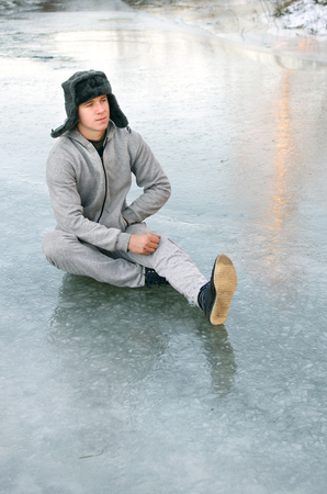 young man in a tracksuit and fur hat sitting on the iceの写真素材