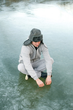 young man in a tracksuit and fur hat sitting on the iceの写真素材
