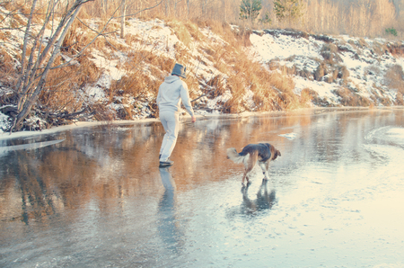 man walks with his dog on the first transparent winter ice, frozen on the surface of the riverの写真素材