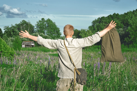 man in an old military uniform with a large bag standing in the field with his arms outstretchedの写真素材