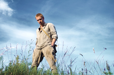 guy in the old military uniform of the second world war in full growth in the field against the cloudy blue skyの写真素材