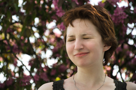 young woman squinting from allergies in a blooming gardenの写真素材