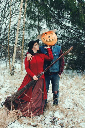 Halloween Scarecrow with a pumpkin on his head and an evil witch with a broom in her hands met in the woodsの写真素材