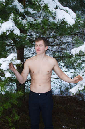 young man without a shirt in the winter forest sprinkles snowの写真素材