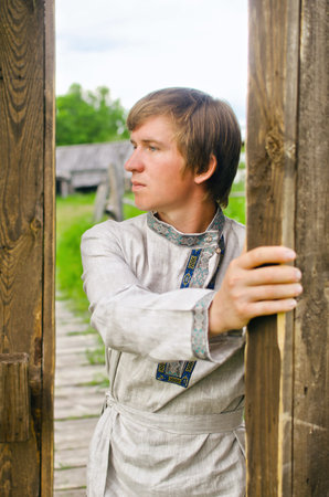 guy in old clothes opens a large wooden gate
