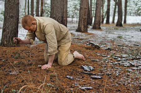 young man in a world war II uniform and barefoot kneels in a winter forestの写真素材