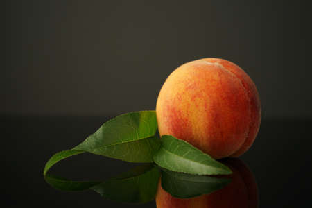 Peach lies on the table against a dark background. Beautiful, juicy, ripe and beautiful is reflected in the black glass of the table. Perfect for backgrounds or wallpapers.の写真素材